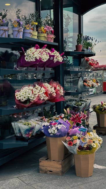 An array of floral arrangements and bouquets displayed on tiered shelves at a flower shop near Stepney Green station. The flowers include white daisies, pink lilies, and purple carnations, wrapped in 